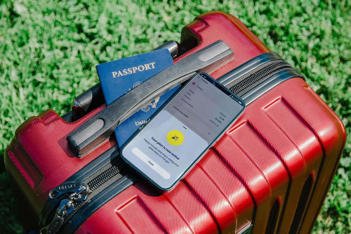 Rode koffer in het gras met een paspoort en een smartphone erop