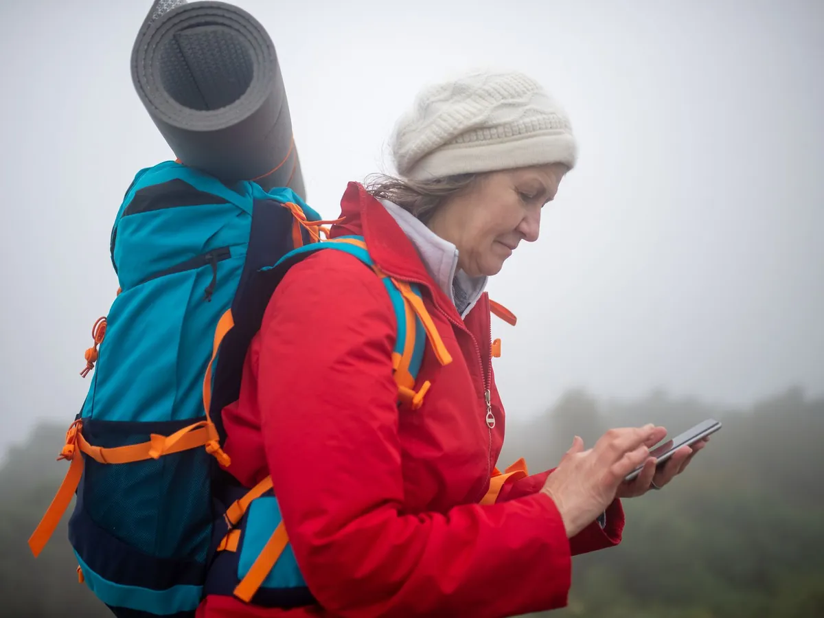 Wandelaarster met rugzak controleert in de mist haar route op een telefoon
