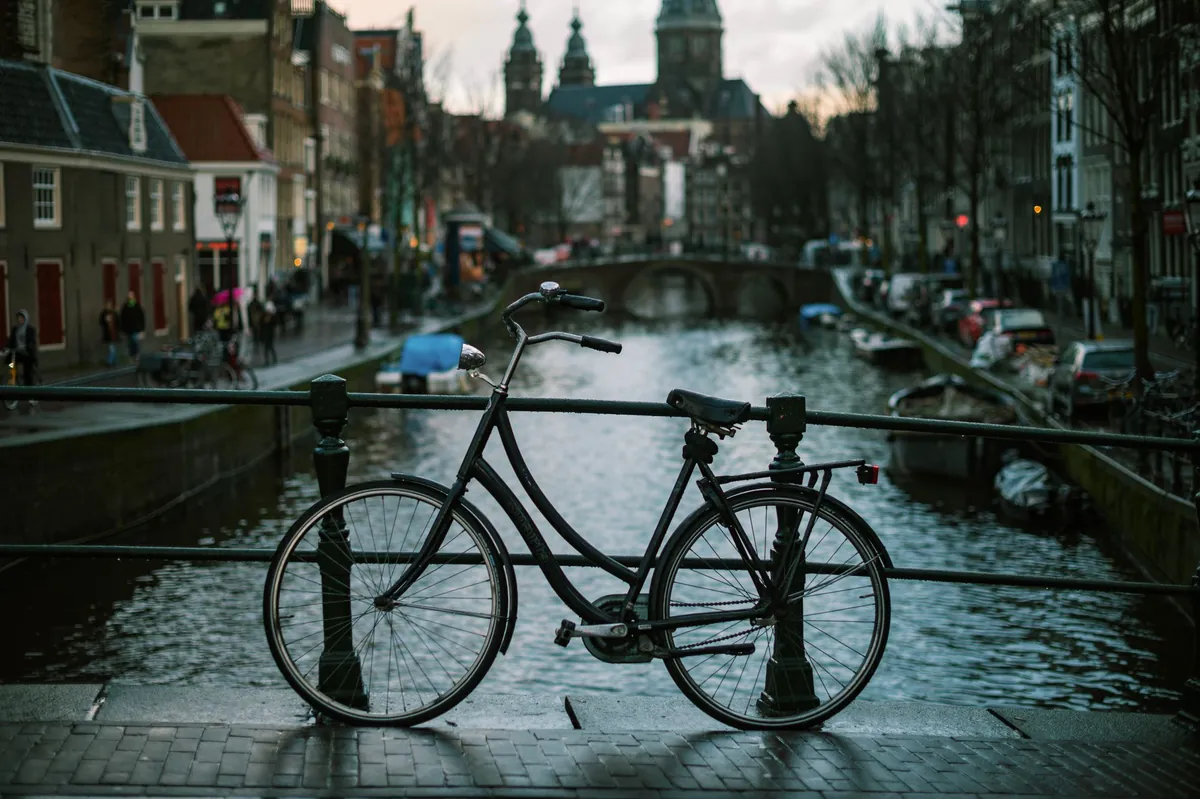 Zwarte fiets geparkeerd tegen een brugleuning aan een Amsterdamse gracht