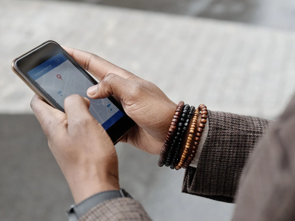 Twee handen met kralenarmbandjes houden een smartphone vast met een kaart en locatiemarkering