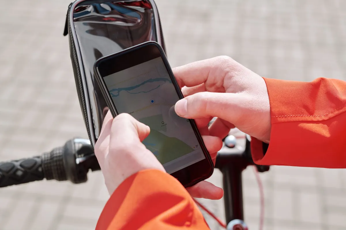 Fietser in oranje jas bedient een smartphone met kaart in een houder op het stuur