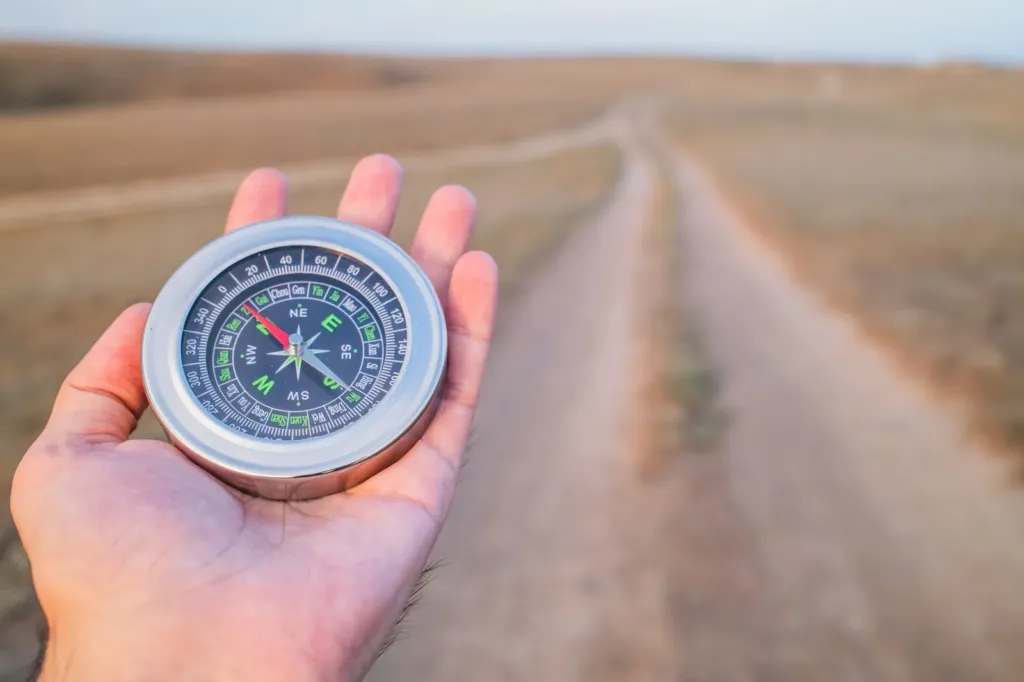 Hand met een kompas boven een zandpad dat door een open landschap loopt