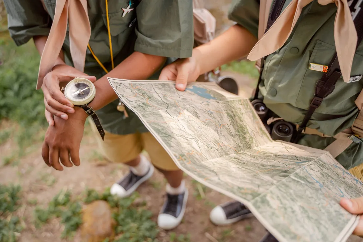 Scouts in uniform bekijken samen een wandelkaart met een kompas om de pols