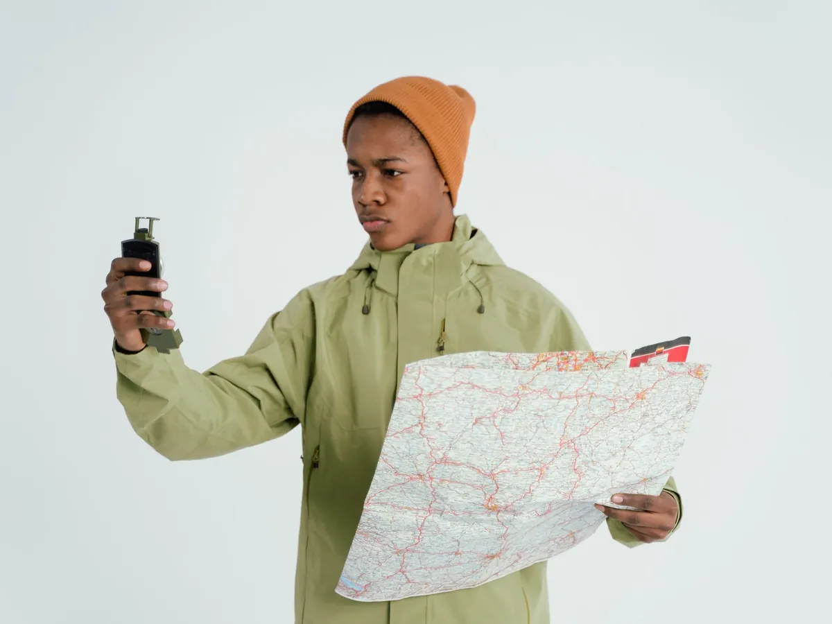 Man in outdoorjas houdt een navigatieapparaat omhoog en heeft een papieren wegenkaart in zijn andere hand