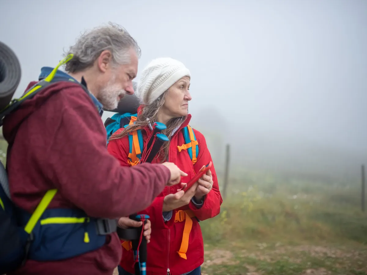 Twee wandelaars met rugzak bekijken samen een telefoon in een mistig heuvellandschap
